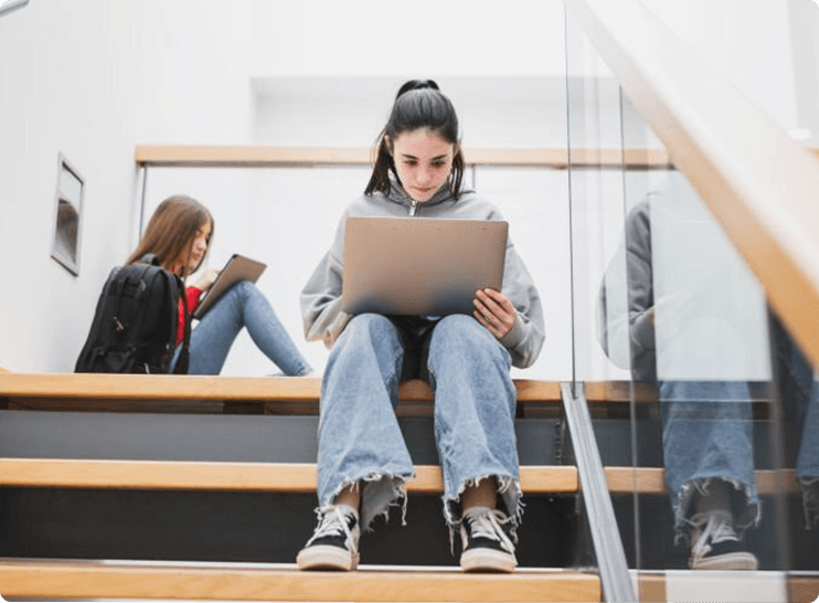 young female students looking at books in school stairs